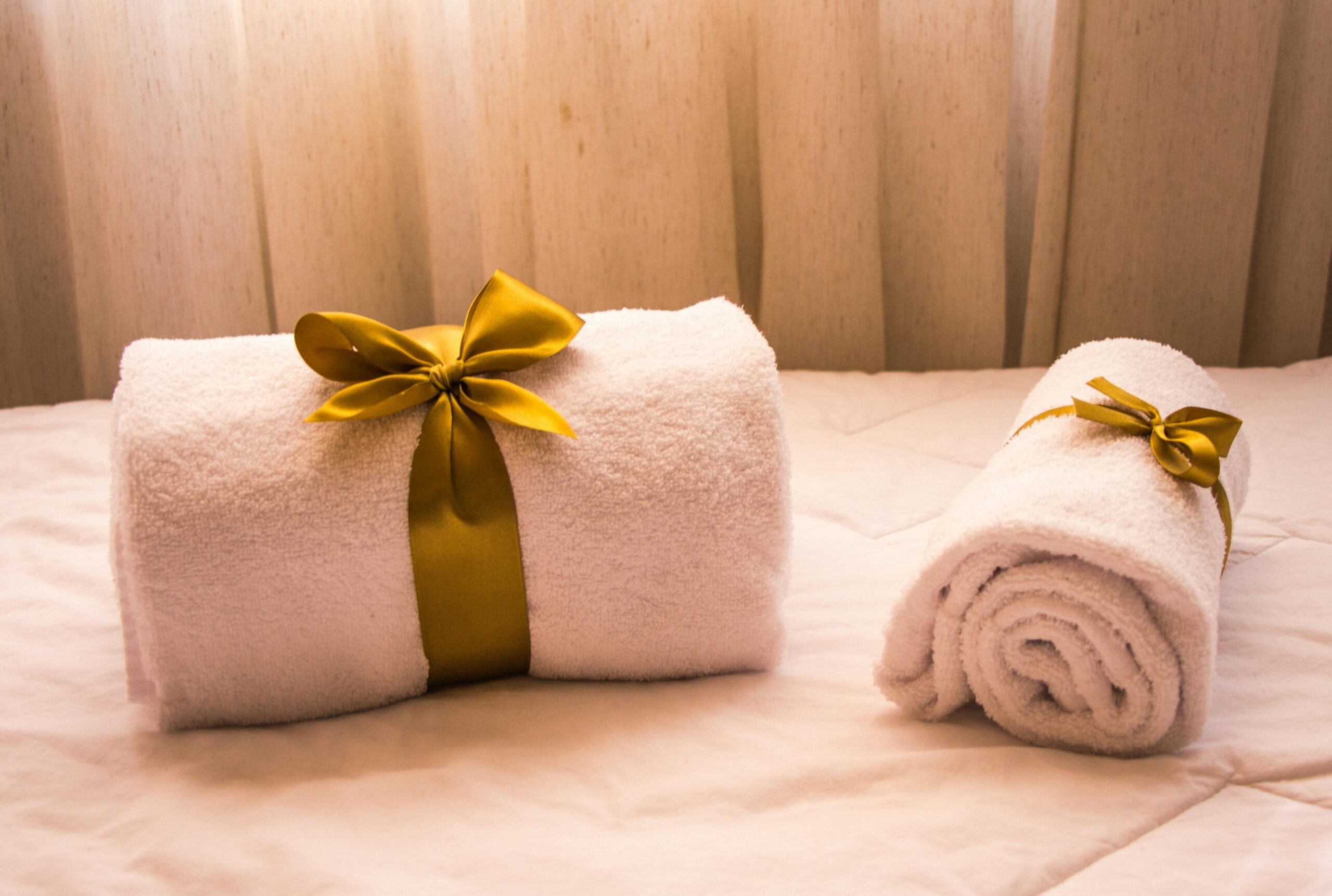 Luxurious white towels adorned with golden ribbons on a bed, creating an elegant and welcoming atmosphere.