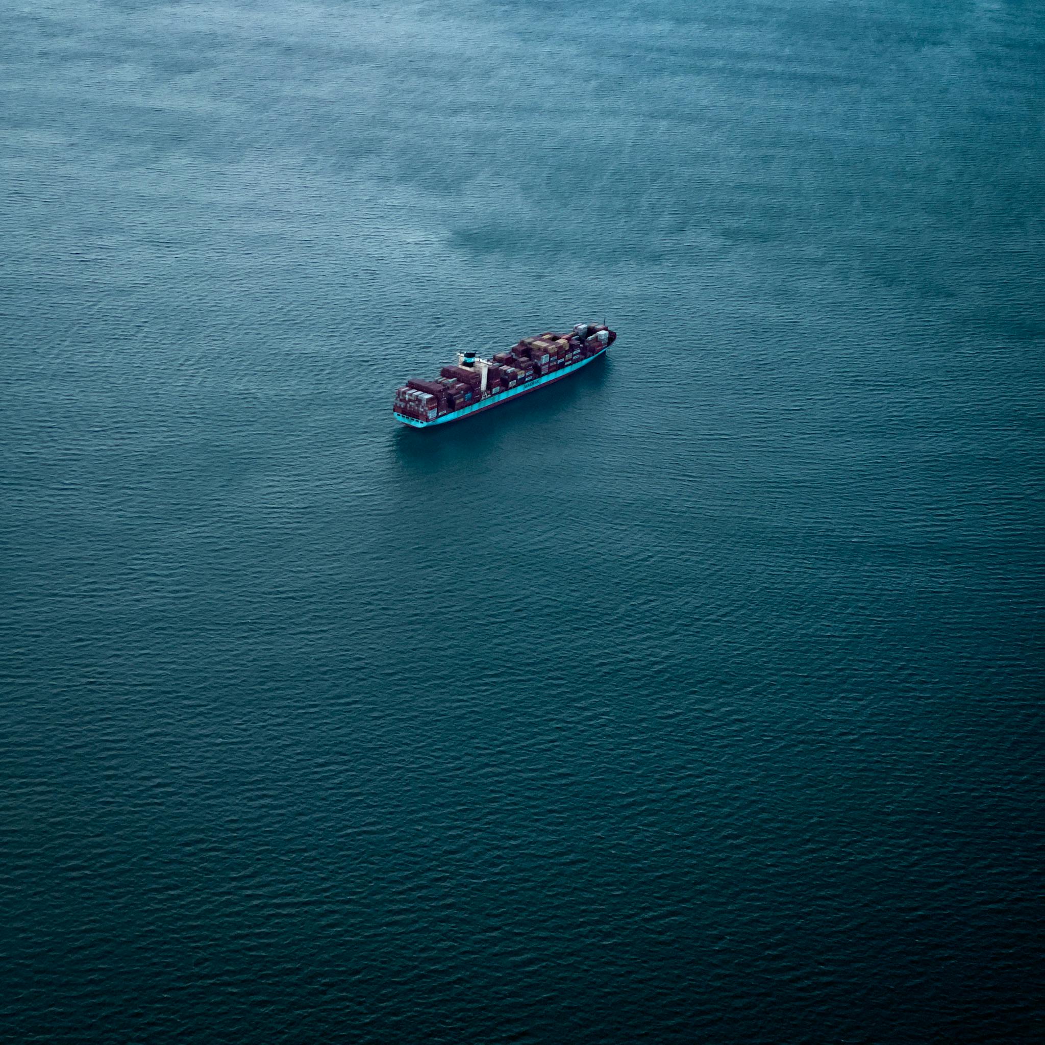 High-altitude shot of a cargo ship navigating vast blue waters.